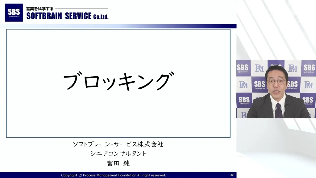 スーツを着た男性が、大きな太字の日本語で「ブロッキング」という文字が書かれたスライドを使ってプレゼンテーションを行っています。背景には、会社のロゴ「ソフトブレーンサービス株式会社」と日本語のテキストが目立つように表示されています。